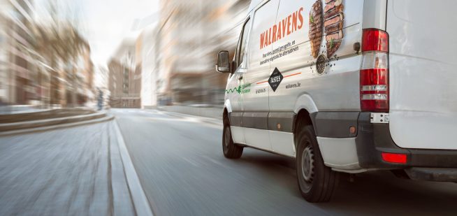 A fast moving white van on a bright street with high buildings. Motion blurred background.
