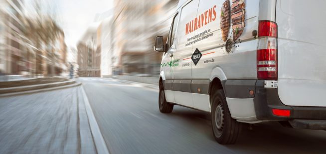 A fast moving white van on a bright street with high buildings. Motion blurred background.