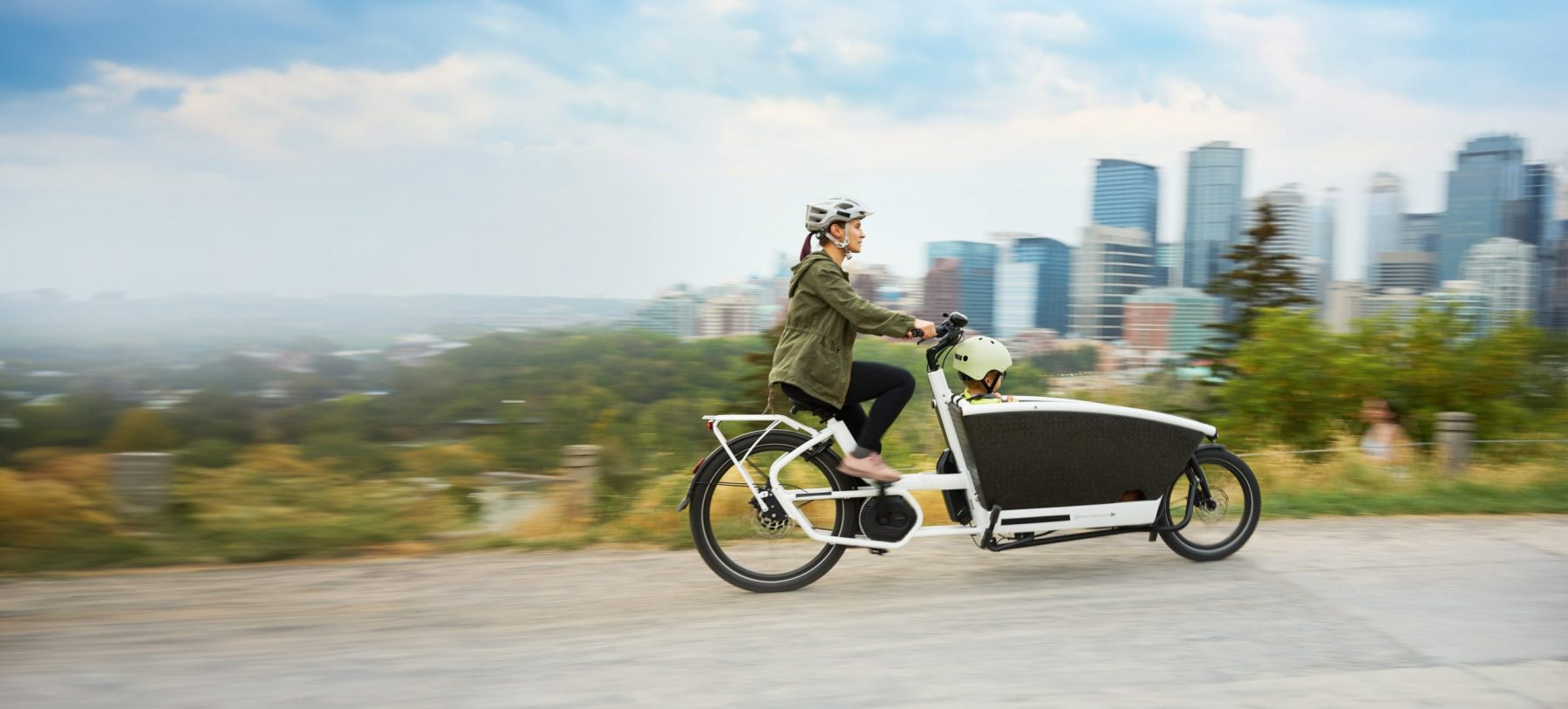 Mom and riding a cargo bike with her young son on a park path